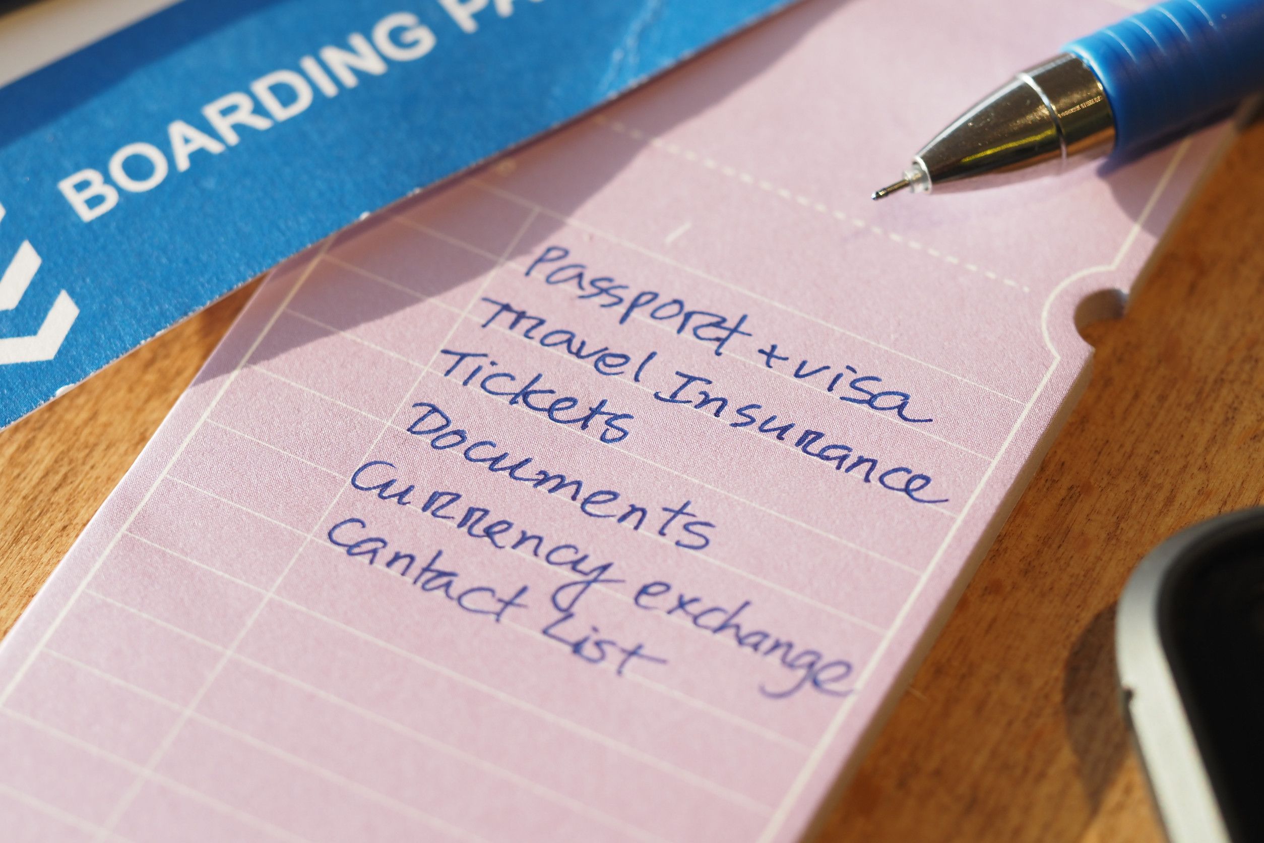 Travel Checklist Next To Boarding Pass And Pen On Wooden Surface